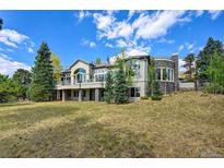 Stunning gray home featuring a stone chimney, rounded tower, walk out basement and balconies, all nestled among mature trees at 814 Neville Ln, Golden, CO 80401