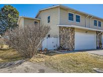 Tan townhome featuring a two-car garage with a stone facade and a white fenced in area at 2446 S Vaughn Way # A, Aurora, CO 80014