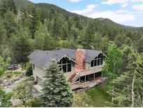 Charming mountain home with a stone chimney, large windows, and a spacious deck surrounded by lush greenery at 2218 Witter Gulch Rd, Evergreen, CO 80439