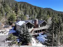 Mountain home featuring a deck, stone chimney, and surrounded by pine trees at 2218 Witter Gulch Rd, Evergreen, CO 80439