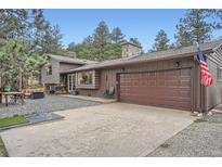 Charming exterior with a two-car garage, gravel driveway, and stone chimney at 2013 Swede Gulch Rd, Evergreen, CO 80439