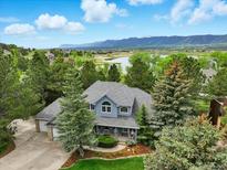 Picturesque aerial view of a two-story home with mature trees, lake, and mountain backdrop at 18590 Lower Lake Rd, Monument, CO 80132