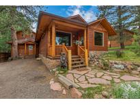Charming log cabin home with a stone pathway and wood porch, nestled among mature trees at 29090 Golf Way, Evergreen, CO 80439