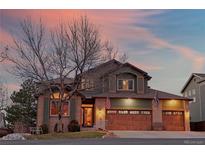 Inviting two-story home featuring a three-car garage, brick accents, and manicured lawn at dusk at 16873 Boreas Ct, Parker, CO 80134