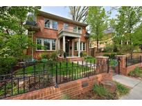 Charming two-story red brick home featuring a welcoming front porch and manicured front yard with wrought iron fence at 535 N High St, Denver, CO 80218