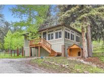 Charming home featuring a wooden porch and stairs, complemented by a matching dog house, set amongst mature trees at 30690 Highway 72, Golden, CO 80403