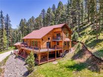 Stunning exterior featuring a wrap-around deck with a beautiful wooden design and surrounded by lush trees at 11768 Black Hawk Dr, Conifer, CO 80433