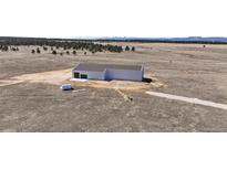 Expansive aerial view of metal building with large plot of land surrounded by mature trees and mountain range backdrop at 14550 Arfsten Rd, Larkspur, CO 80118