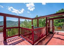Red wooden deck with views of treed mountains and a bright blue sky with fluffy white clouds at 32392 Lodgepole Dr, Evergreen, CO 80439