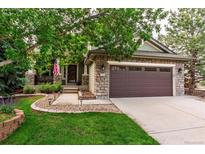 Charming home featuring a stone facade, covered porch, well-manicured lawn, and an attached two-car garage at 9882 S Hoyt Ct, Littleton, CO 80127
