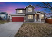 Charming two-story home with a red garage door, welcoming porch, and well-maintained lawn at 12243 N Ivanhoe Cir, Brighton, CO 80602