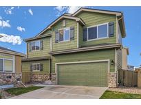 Two-story green home featuring a two-car garage, stone accents, and well-maintained landscaping at 10117 Wyandott N Cir, Thornton, CO 80260
