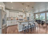 Well-lit kitchen features white cabinets, stainless appliances, hardwood floors, and a breakfast bar with pendant lighting at 23957 E Rocky Top Ave, Aurora, CO 80016