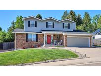 Charming two-story home featuring brick and gray siding, manicured lawn, and a vibrant red front door at 7822 W Ottawa Pl, Littleton, CO 80128