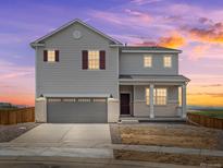 Two-story home featuring a gray exterior, brick accents, and a two-car garage under a beautiful evening sky at 8819 Sedalia St, Commerce City, CO 80022