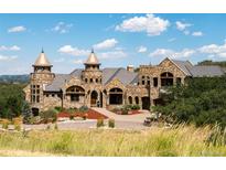 Majestic stone castle-like home with copper-topped turrets and a meticulously landscaped yard under a blue sky at 3120 Bears Den Dr, Sedalia, CO 80135