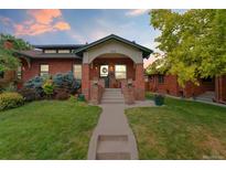 Charming brick home featuring a covered front porch, manicured lawn, and lush landscaping at 1215 Jackson St, Denver, CO 80206