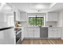 Bright kitchen featuring white cabinets, stainless steel appliances, and a window with a view of the trees at 12662 E Warren Dr # F, Aurora, CO 80014