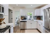 Bright kitchen features white cabinets, stainless appliances, and view into adjacent bathroom at 5147 Saint Paul St, Denver, CO 80216