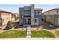 Contemporary two-story home featuring a stone chimney, well-manicured lawn, and inviting front porch with seating at 10062 Southlawn Cir, Commerce City, CO 80022