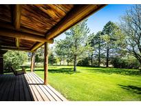 Covered porch with wooden flooring and a swing overlooks the expansive lawn and trees at 2965 Wagner St, Strasburg, CO 80136