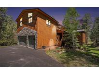 Charming two-story home showcasing a stone facade garage, wood siding, and mature trees at 8722 S Ault Ln, Morrison, CO 80465