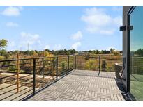 A rooftop deck with gray tile flooring has black metal railings and a lovely view of the surrounding trees and blue sky at 1232 N Tennyson St, Denver, CO 80204
