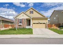 Inviting yellow two-story home with a stone facade and a two-car garage at 16076 Columbine Pl, Thornton, CO 80602