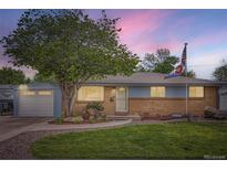 Charming brick home with well-maintained lawn, mature tree, and walkway, accented with a Colorado State flag at 6761 Harlan St, Arvada, CO 80003