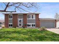 Two-story home features a brick and gray wood facade, lush front yard, and attached two-car garage at 12235 Garfield Pl, Thornton, CO 80241