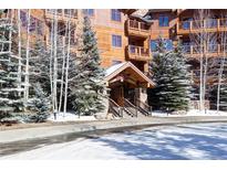 Inviting lodge entrance with wood and stone features, surrounded by snow-covered evergreens and birch trees at 50 Mountain Thunder Dr # 1212, Breckenridge, CO 80424