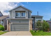 Two-story home featuring a two-car garage, a basketball hoop, and a well-maintained lawn with a young tree and blue sky at 4935 Apollo Bay Dr, Highlands Ranch, CO 80130