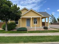 Charming yellow house featuring a cozy covered porch, well-maintained lawn, and mature landscaping at 55619 E 31St Ave, Strasburg, CO 80136