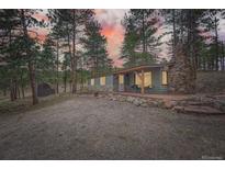 Charming home featuring a stone chimney and a covered porch surrounded by tall trees and a gravel driveway at 3989 S Palo Verde Rd, Evergreen, CO 80439
