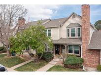 Charming townhome with well-manicured lawn, mature trees and a brick chimney under a partly cloudy sky at 9620 W Chatfield Ave # D, Littleton, CO 80128