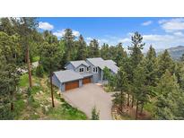 Stunning two-story home with a three-car garage surrounded by lush greenery and a long driveway at 6637 Berry Bush Ln, Evergreen, CO 80439