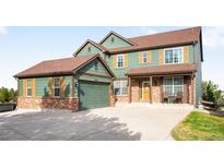 Charming two-story home showcasing green siding, brick accents, well-manicured lawn and covered porch at 23427 Song Bird Hills Pl, Parker, CO 80138