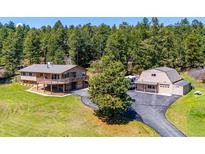 Sprawling property featuring multiple buildings, a circular driveway, lush lawn, and views of surrounding trees at 8045 S Wagon Wheel Rd, Morrison, CO 80465
