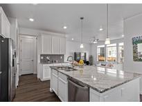 Open kitchen area with a granite island and stainless appliances leads into the living room with dark hardwood floors at 723 176Th Ave, Broomfield, CO 80023