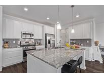 Bright kitchen features white cabinets, stainless steel appliances, a large island with a stone countertop, and modern pendant lighting at 723 176Th Ave, Broomfield, CO 80023