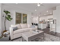 Bright living room with a neutral palette, modern ceiling fan, and dark hardwood floors flowing into the kitchen area at 723 176Th Ave, Broomfield, CO 80023