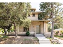 Charming brick two-story home with covered front porch and mature trees providing shade at 3330 Bruce Randolph Ave, Denver, CO 80205