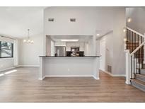 Open-concept living room view to kitchen with bar, and staircase with wood-look flooring and neutral walls at 540 S Forest St # 3-204, Denver, CO 80246