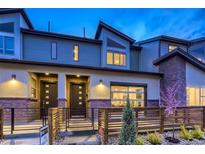 Stylish townhome featuring modern design, a mix of brick and siding, and an inviting fenced front yard at twilight at 12339 W 58Th Ct, Arvada, CO 80004