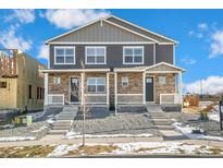 Traditional-style home featuring stone accents, gray siding, and a charming front porch with white railing at 18714 E 99Th Ave, Commerce City, CO 80022