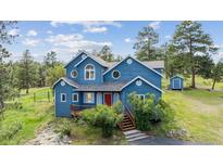 Charming blue two-story home with red door, wooden porch and stairs, and lush green landscaping on a sunny day at 5939 S Skyline Dr, Evergreen, CO 80439