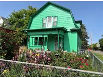 Charming two-story home with a bright green exterior and flourishing flower garden in front at 4047 Lowell Blvd, Denver, CO 80211