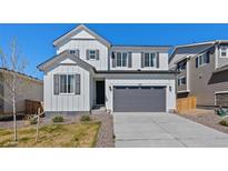Charming two-story home with white siding, a gray garage door, and well-maintained landscaping at 9175 Uravan Ct, Commerce City, CO 80022