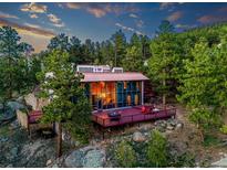 Stunning modern house surrounded by lush greenery and trees, featuring a deck and a wall of windows at 8791 Grizzly Way, Evergreen, CO 80439