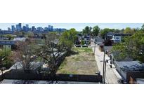 A vacant lot is surrounded by a wooden fence and lush trees, offering a serene setting with a city skyline backdrop at 1735 W 37Th, Denver, CO 80211